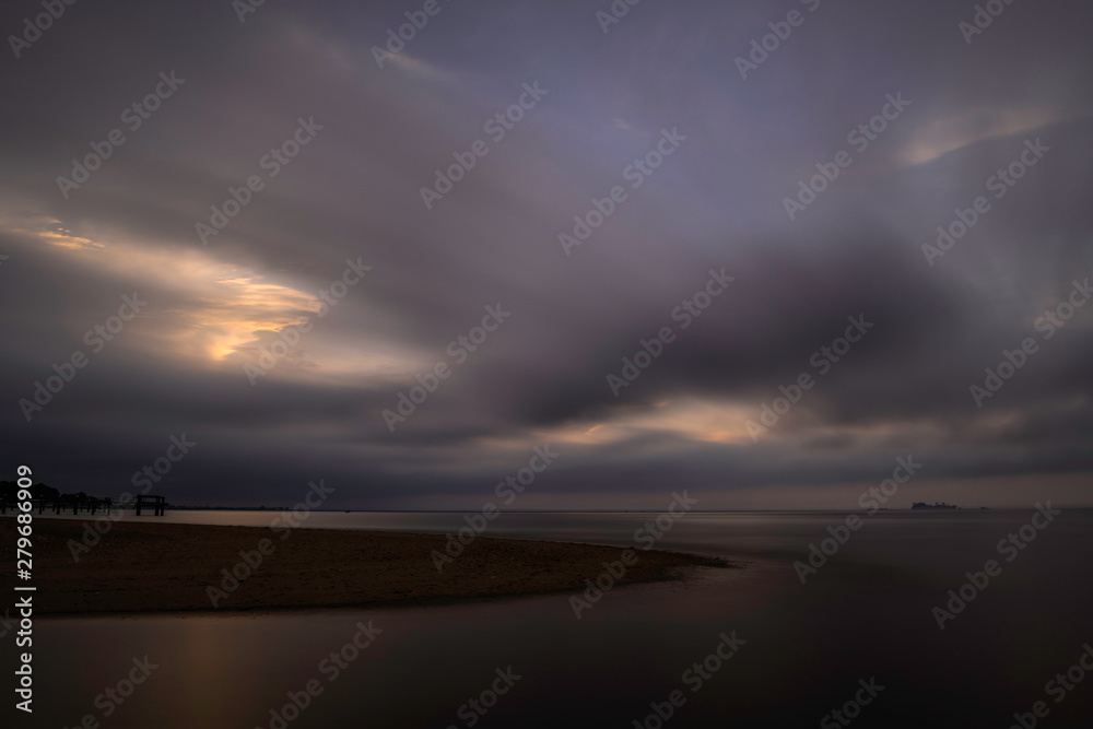 Dramatic sunset over Atlantic Highlands beach in New Jersey, featuring moody sky on the background. Shot using slow shutter speed