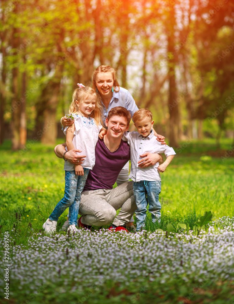 Fototapeta premium Portrait of family having fun in flowering city park on bright sunny day happily spending their leisure time together outdoors