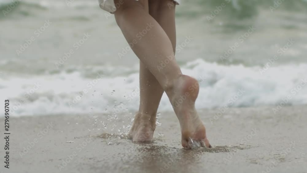 Female legs stepping on sandy beach approaching sea water close up slow motion. Faceless woman walking on coastline by ocean relaxing natural light copy space. Relaxation travel summer vacation Female legs stepping on sandy beach approaching sea water close up slow motion. Faceless woman walking on coastline by ocean relaxing natural light copy space. Relaxation travel summer vacation
