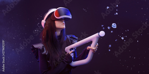Beautiful woman in futuristic dress over dark blue magic light background. Gamer girl in glasses of virtual reality with controller in hands. Augmented reality, game, hobby concept. VR.