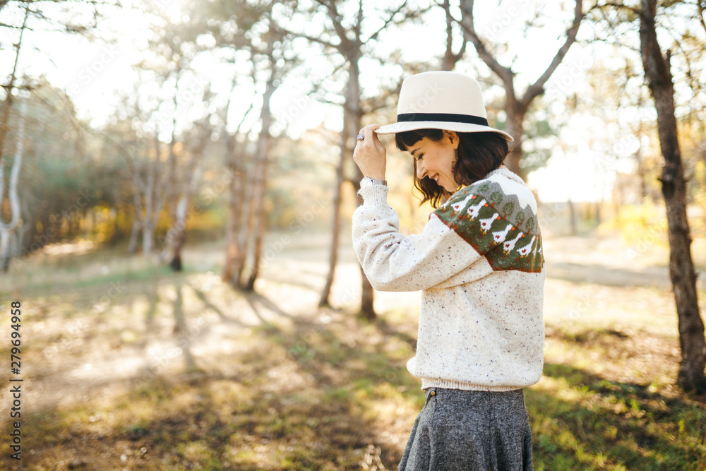 Lovely girl with a beautiful smile at sunset in the forest. The girl is dressed with a hat, a light sweater and a skirt. Knee-high boots. Hipster girl concept, lifestyle style, autumn style. Lovely girl with a beautiful smile at sunset in the forest. The girl is dressed with a hat, a light sweater and a skirt. Knee-high boots. Hipster girl concept, lifestyle style, autumn style.