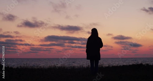 Back view of silhouetted woman staring at sea sunset alone at seaside slow motion. Girl traveler standing at seaside backlit by natural evening light outdoors. Stress overcome depression tranquilizers