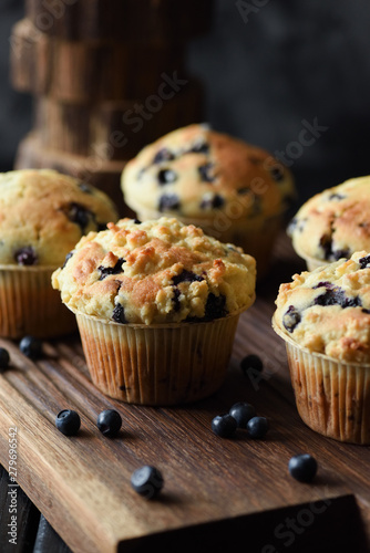 Homemade crumble top blueberry muffins with raw berries on oak cutting board. Low key still life with natural lighting