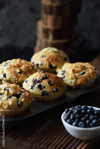 Homemade crumble top blueberry muffins with raw berries on black background. Low key still life with natural lighting