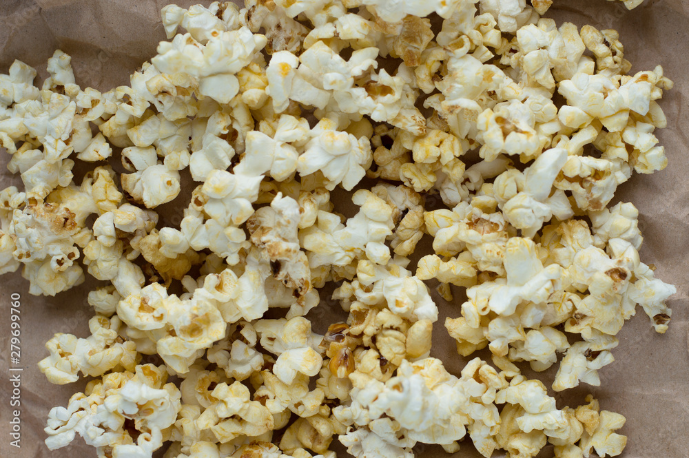 Homemade vegan fresh crunchy popcorn on brown craft paper lie on a dark wooden table. A useful snack for a movie, an idea for a meal. Close-up, top view. Homemade vegan fresh crunchy popcorn on brown craft paper lie on a dark wooden table. A useful snack for a movie, an idea for a meal. Close-up, top view.