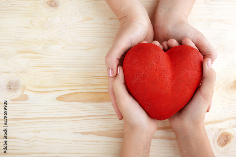 Family holding big red heart in hands on wooden background Family holding big red heart in hands on wooden background