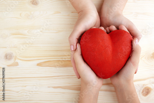 Family holding big red heart in hands on wooden background