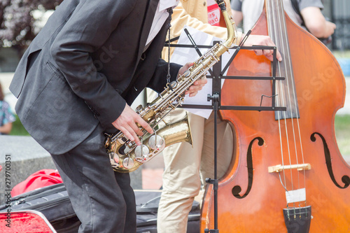 Street musician's hands playing saxophone and double-bass in an urban environment.