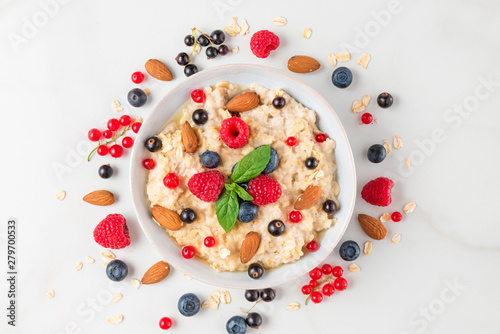 bowl of oatmeal porridge with fresh berries, nuts and mint for healthy diet breakfast on white marble table