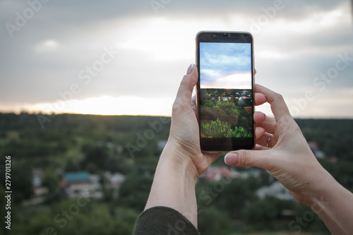 Close-up of female hands shoot a beautiful landscape with green hills and sunset on a smartphone, selective focus