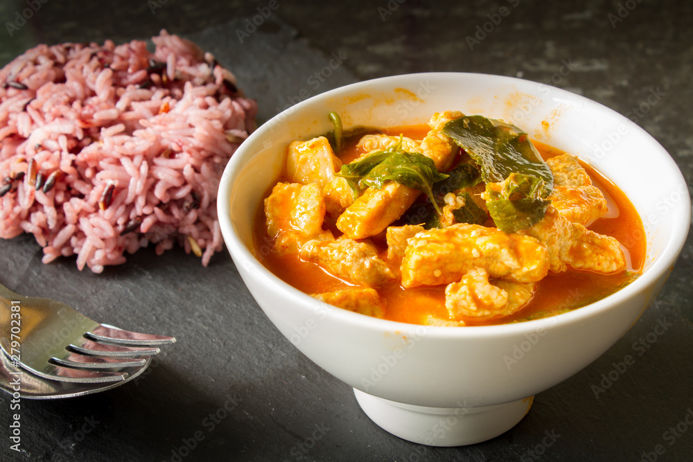 Thai red curry with pork and fresh basil in a white bowl with white and brown rice. Thai red curry with pork and fresh basil in a white bowl with white and brown rice.