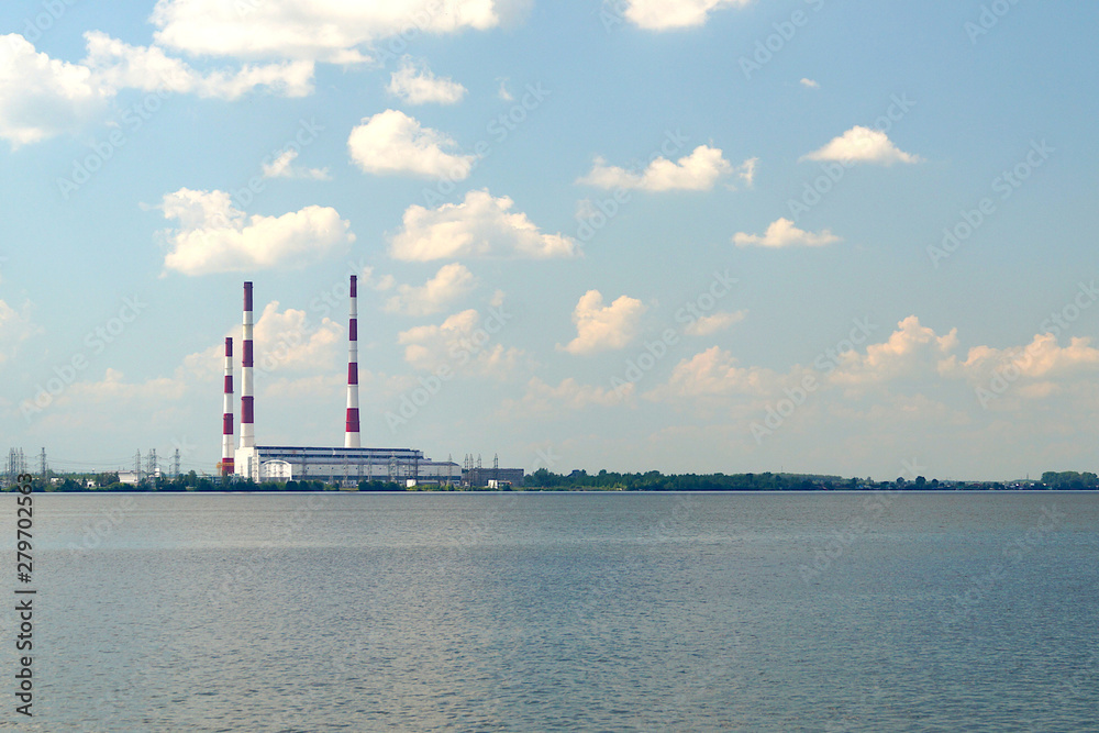 Condensation power plant with high pipes on the shore of a large lake under a blue sky with white clouds.
