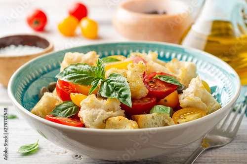 Traditional Italian salad Panzanella with cherry tomatoes, bread, capers and basil in bowl on wooden table. Selective focus.