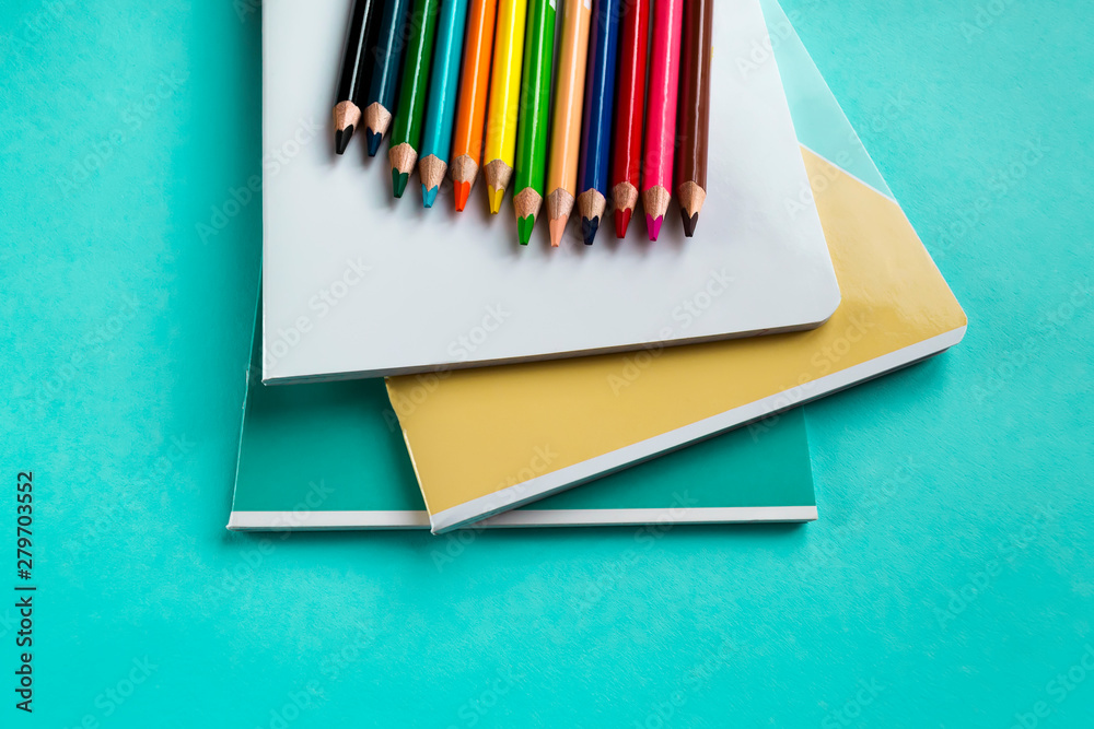 Fototapeta premium Set of exercise books and colored pencils on a green background with space for text. School accessories. Flat lay