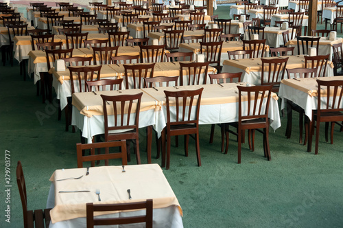 rows of wooden tables and chairs in the restaurant are covered with a tablecloth