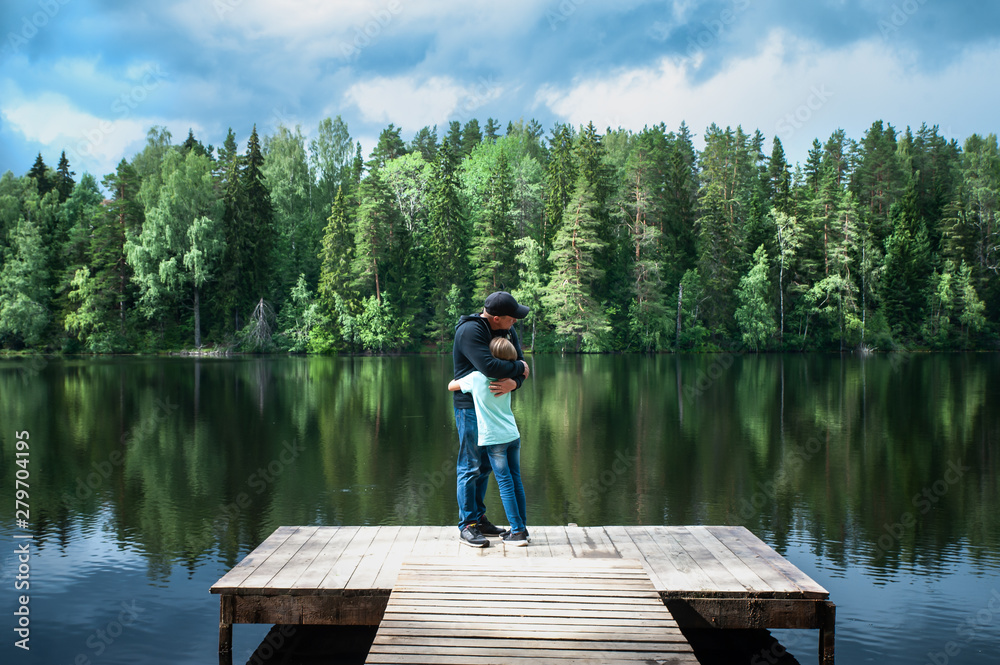 Father and his little daughter stand embracing on the pier of a beautiful lake. Father and daughter relationship concept, father's day..Family love Father and his little daughter stand embracing on the pier of a beautiful lake. Father and daughter relationship concept, father's day..Family love