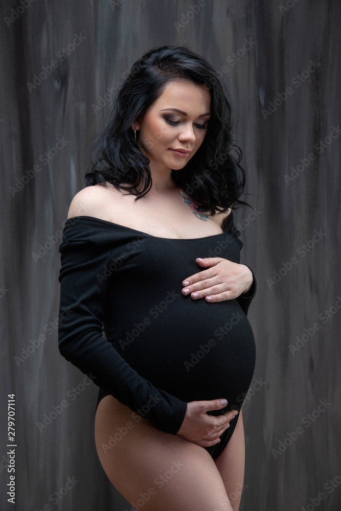 A beautiful young pregnant brunette woman in a black jumpsuit is hugging her tummy. Stylish pregnancy, women's health, happy motherhood A beautiful young pregnant brunette woman in a black jumpsuit is hugging her tummy. Stylish pregnancy, women's health, happy motherhood
