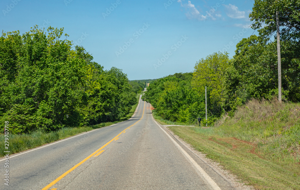 Empty long highway going up a green hill in a sunny spring day