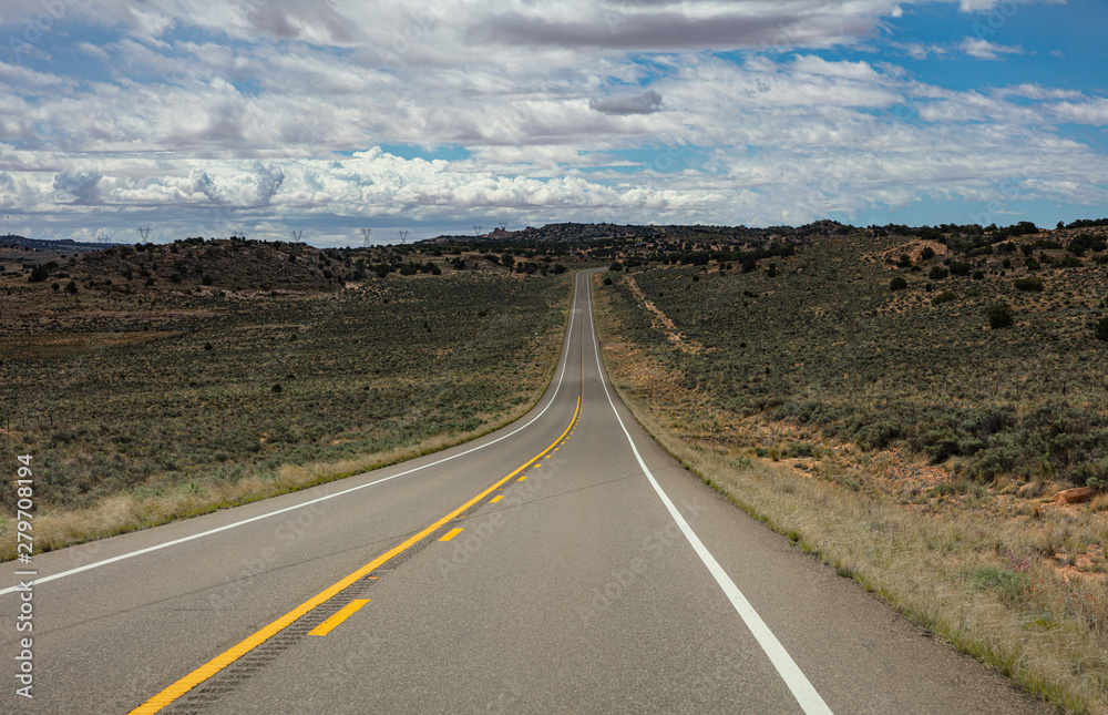 Long highway in the american countryside, cloudy blue sky
