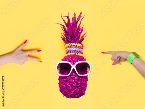Pineapple in glasses and woman hаnds on a yellow background