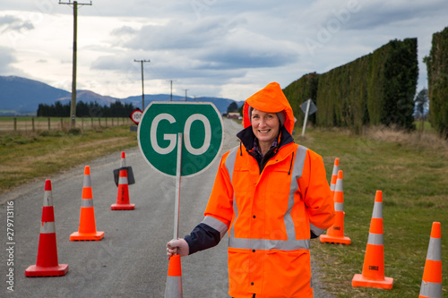 A female on a road crew operates a road sign and traffic cones at a hazard area on a rural country road in New Zealand