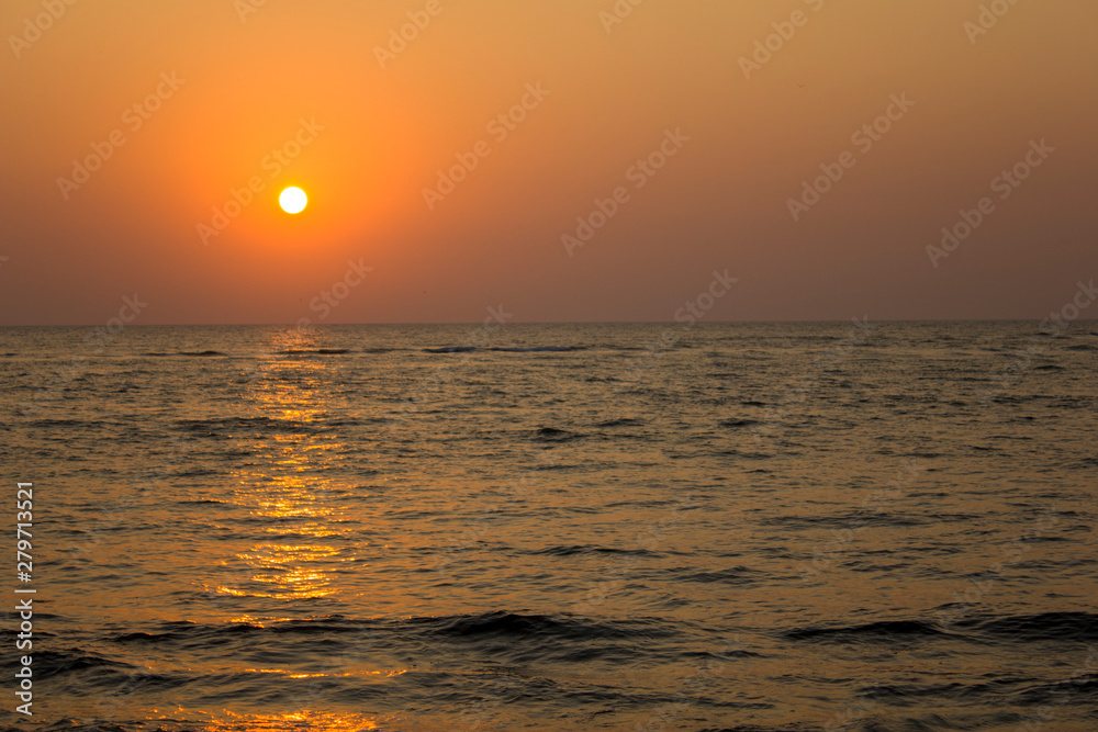 evening ocean with a sun path and waves against the backdrop of a dark yellow, purple sunset sky