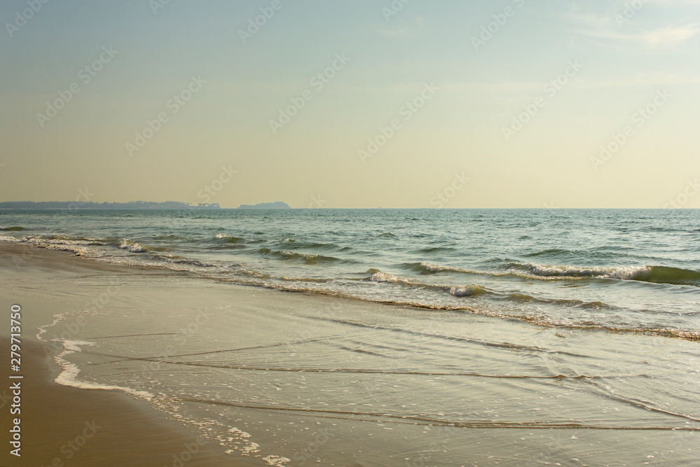 yellow sandy beach against the backdrop of the foam of the ocean waves under a clear sky