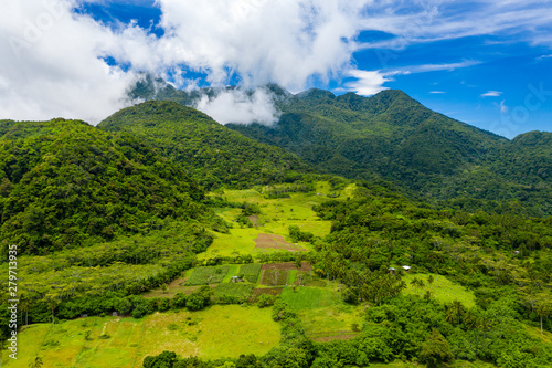 Aerial drone view of clouds passing over lush greenfarmland with mountains and volcanos in the background  Camiguin  Philippines 