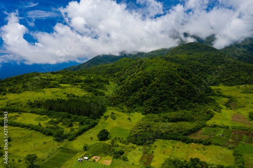 Aerial drone view of clouds passing over lush greenfarmland with mountains and volcanos in the background (Camiguin, Philippines) photo