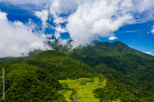 Aerial drone view of clouds passing over lush greenfarmland with mountains and volcanos in the background (Camiguin, Philippines)