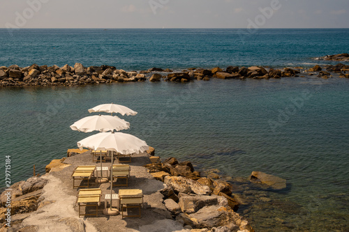 High angle view of a rocky reef with white sun umbrellas and beach loungers in a bay sheltered by a breakwater, Oneglia, Imperia, Liguria, Italy photo