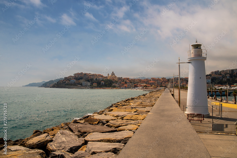 Scenic view of the quayside with rocky breakwater, a white lighthouse and the old sea borough Parasio on the promontory in the background in a sunny summer day, Porto Maurizio Imperia, Liguria, Italy