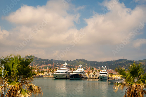 High angle view of the harbor of the sea town with moored luxury yachts and top of palm trees in the foreground in summer, Porto Maurizio, Imperia, Liguria, Italy © Simona Sirio