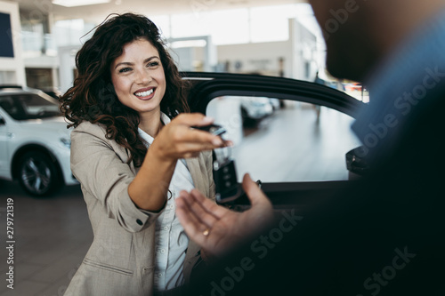 Happy middle age businessman buying new and expensive car. Beautiful female dealer gives him vehicle keys.