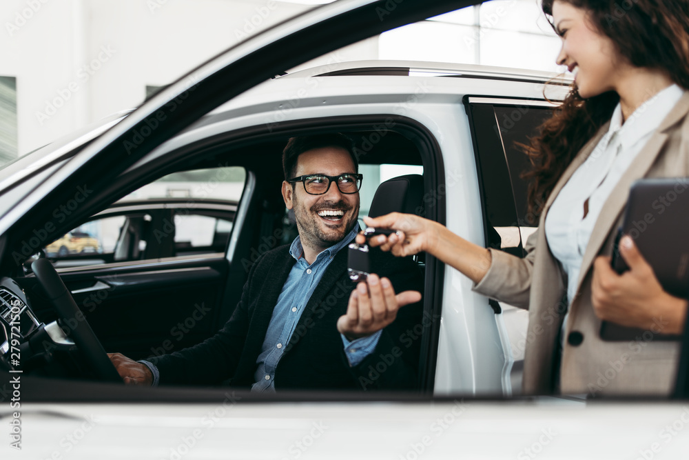 Happy middle age businessman buying new and expensive car. Beautiful female dealer gives him vehicle keys. Happy middle age businessman buying new and expensive car. Beautiful female dealer gives him vehicle keys.