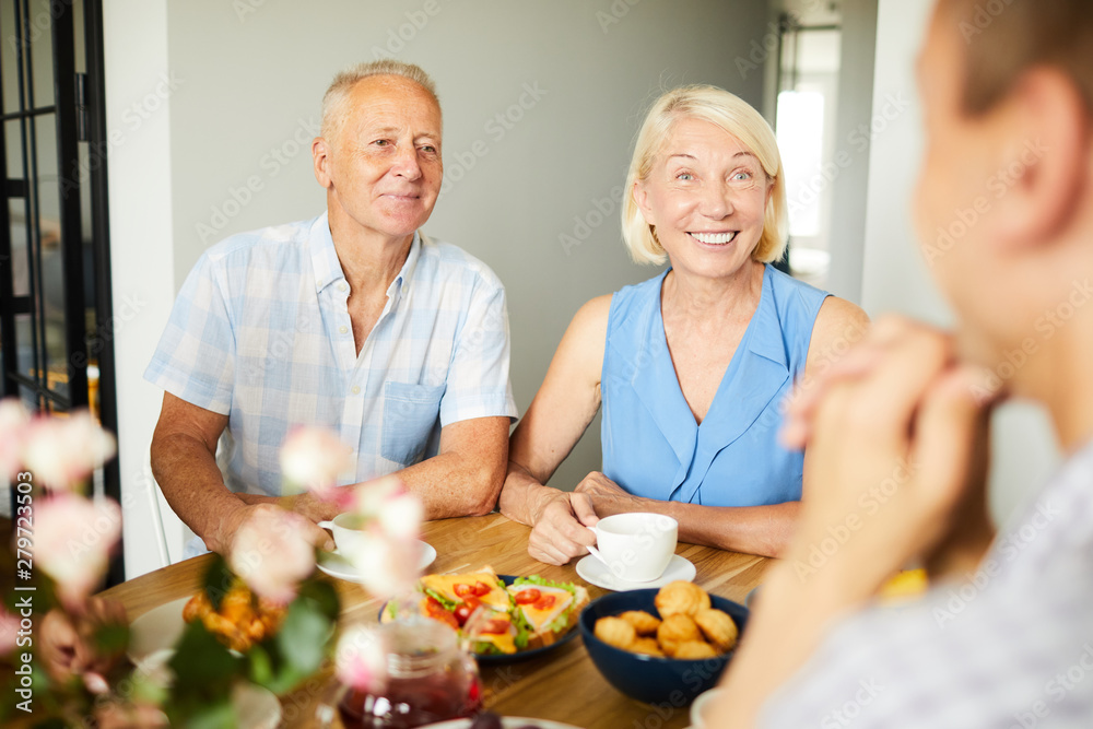 Portrait of smiling mature couple sitting at dinner table with friends and family, copy space