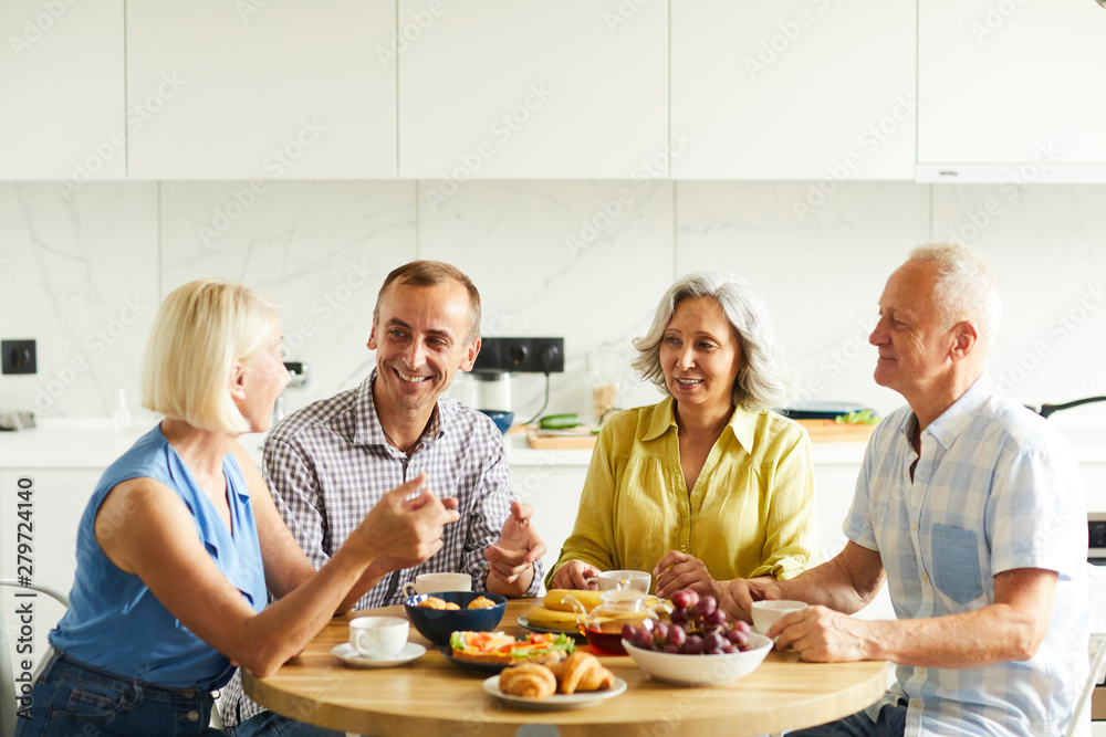 Group of cheerful senior people enjoying lunch while sitting around table in kitchen, copy space