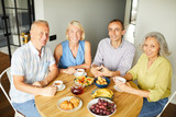 Group of cheerful senior people smiling at camera while sitting around table in kitchen, copy space