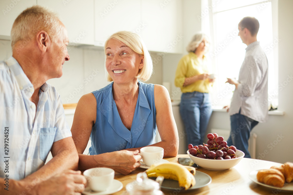 Portrait of happy adult couple looking at each other tenderly while siting at kitchen table in sunlight, copy space Portrait of happy adult couple looking at each other tenderly while siting at kitchen table in sunlight, copy space