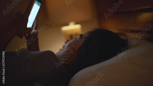 excited young asian woman in bed using cell phone. happy social media user