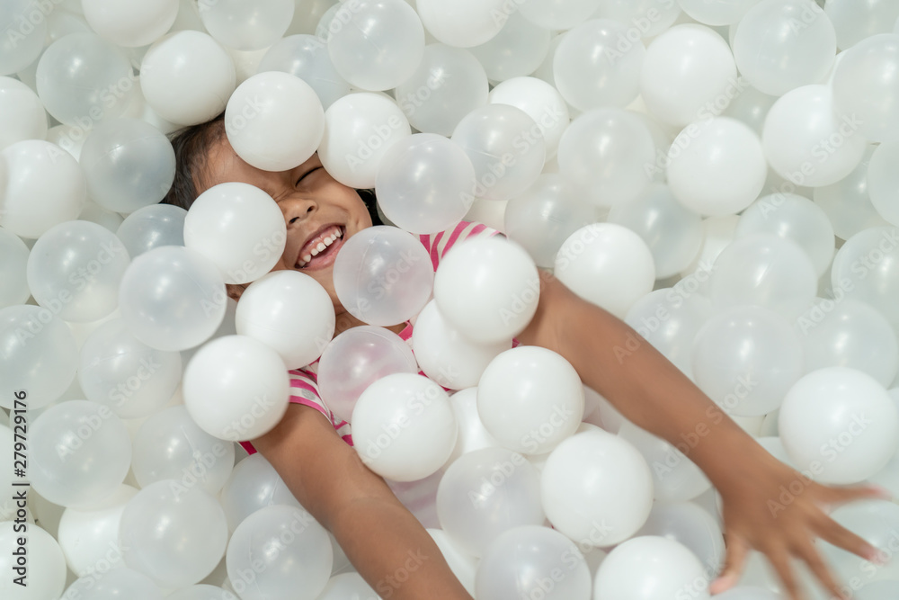 Happy cute asian child girl having fun to play with white plastic balls in the playground Happy cute asian child girl having fun to play with white plastic balls in the playground