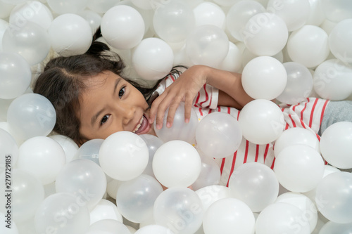 Happy cute asian child girl having fun to play with white plastic balls in the playground photo