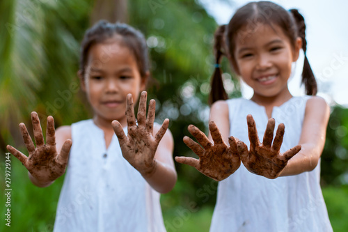 Two cute asian child girls showing dirty hands after planting the tree together in the garden
