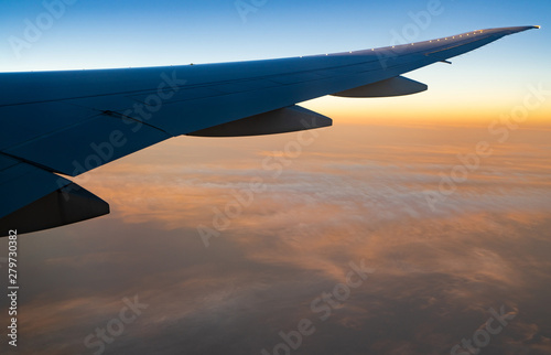Wing of plane over white clouds. Airplane flying on sunrise sky. Scenic view from airplane window. Commercial airline flight. Plane wing above clouds. Flight mechanics concept. International flight.