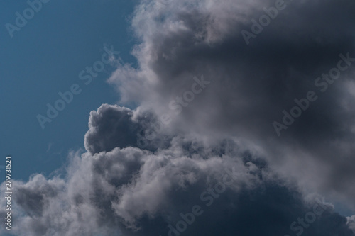 dark thick cloudy formation on the blue sky back lit by the sun light texture background