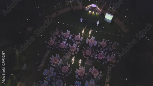 Drone flying over wedding dinner decoration, or marriage anniversary, in the garden outdoor, catering setting chairs and tables, aerial view. Tropical decor style atmosphere.