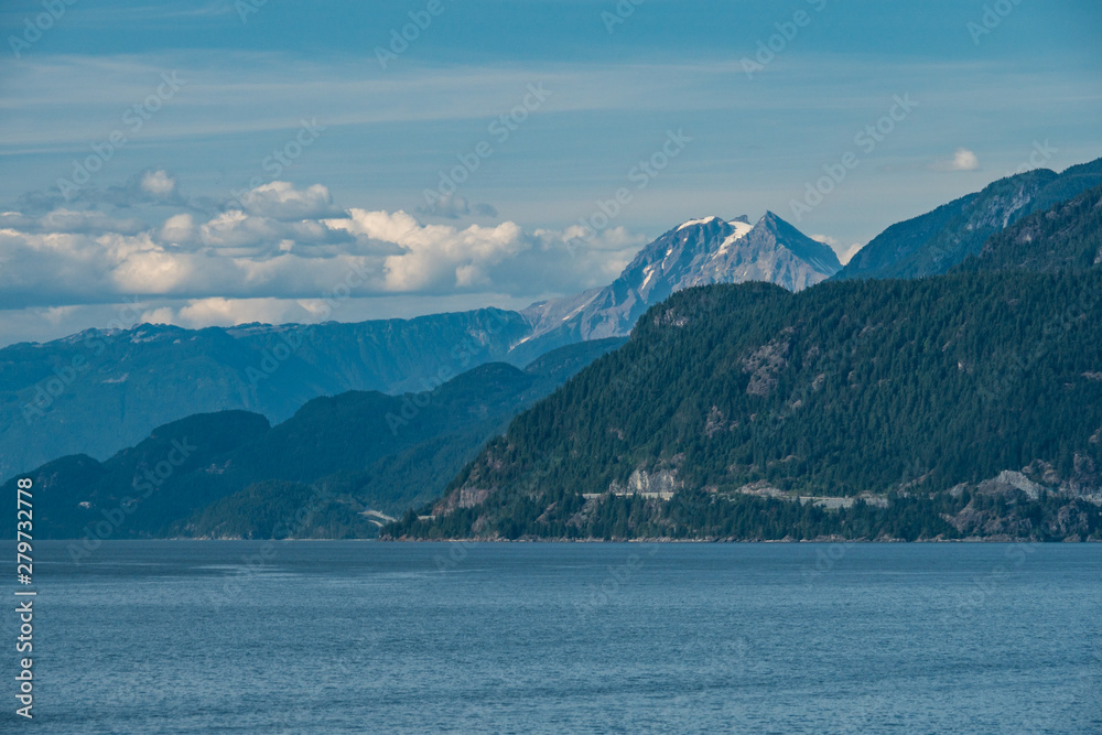 layers of mountains on the island with bit of snow still on the highest peak over the horizon on the ocean under cloudy blue sky