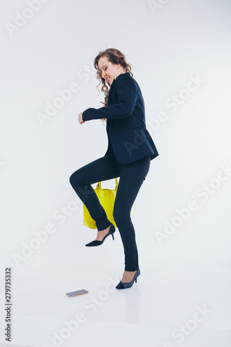 girl puts a foot on the phone. the heel breaks a smartphone. Businesswoman went crazy. Close up on white background. yellow bag