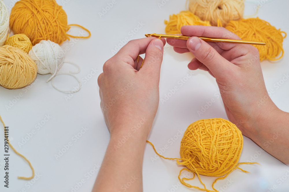 girl knits crochet, on a white background, the process of knitting close-up, yellow ball of thread