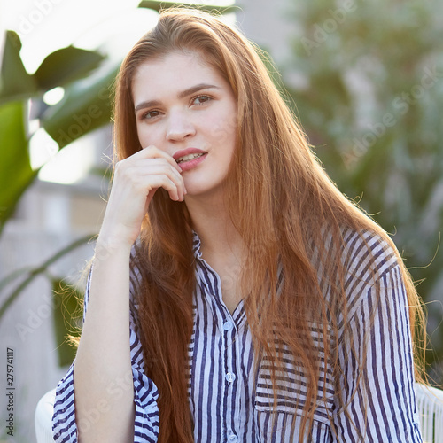 Portrait of young girl sits in the white armchair against blurred balckground